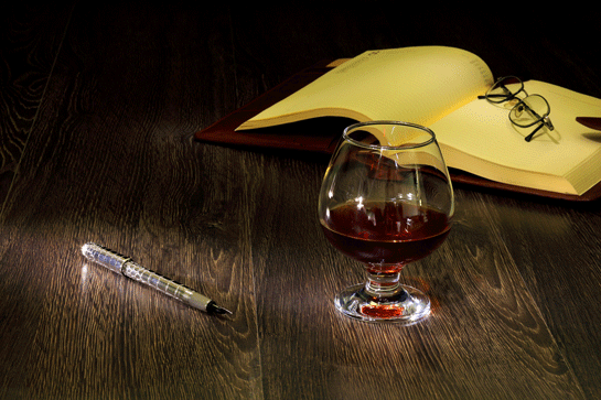 glass of red wine, eye glasses on open book, pen on table